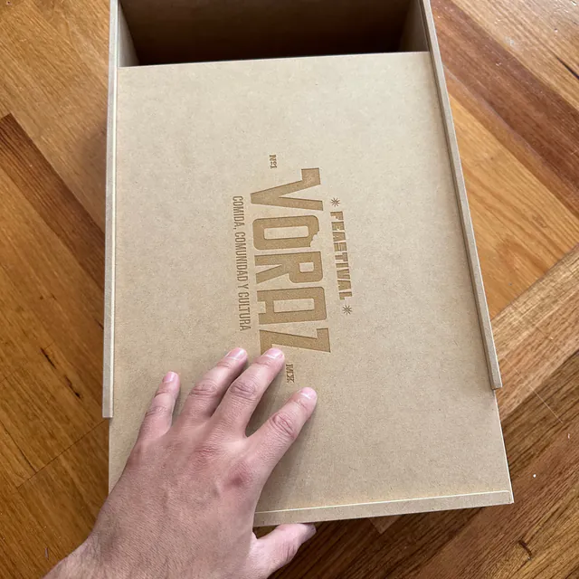 Caja con la tapa deslizada hacia abajo, con un logotipo grabado, y una mano sobre ella